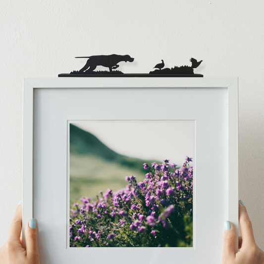 An English pointer flushing grouse ornament made from recycled plastic displayed on top of a picture frame